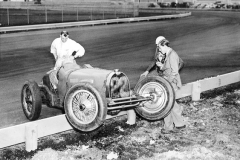  159A Type 59 Vanderbuilt Cup, Roosevelt Raceway, Long Island, New York. October 1936. Driver Louis Meyer (hidden) put the Bugatti spare car over the barrier during one of the practice sessions. Mechanic Robert Aumaitre surveys the damage. See also pictures 151A, 155, 156, 157 & 158A.